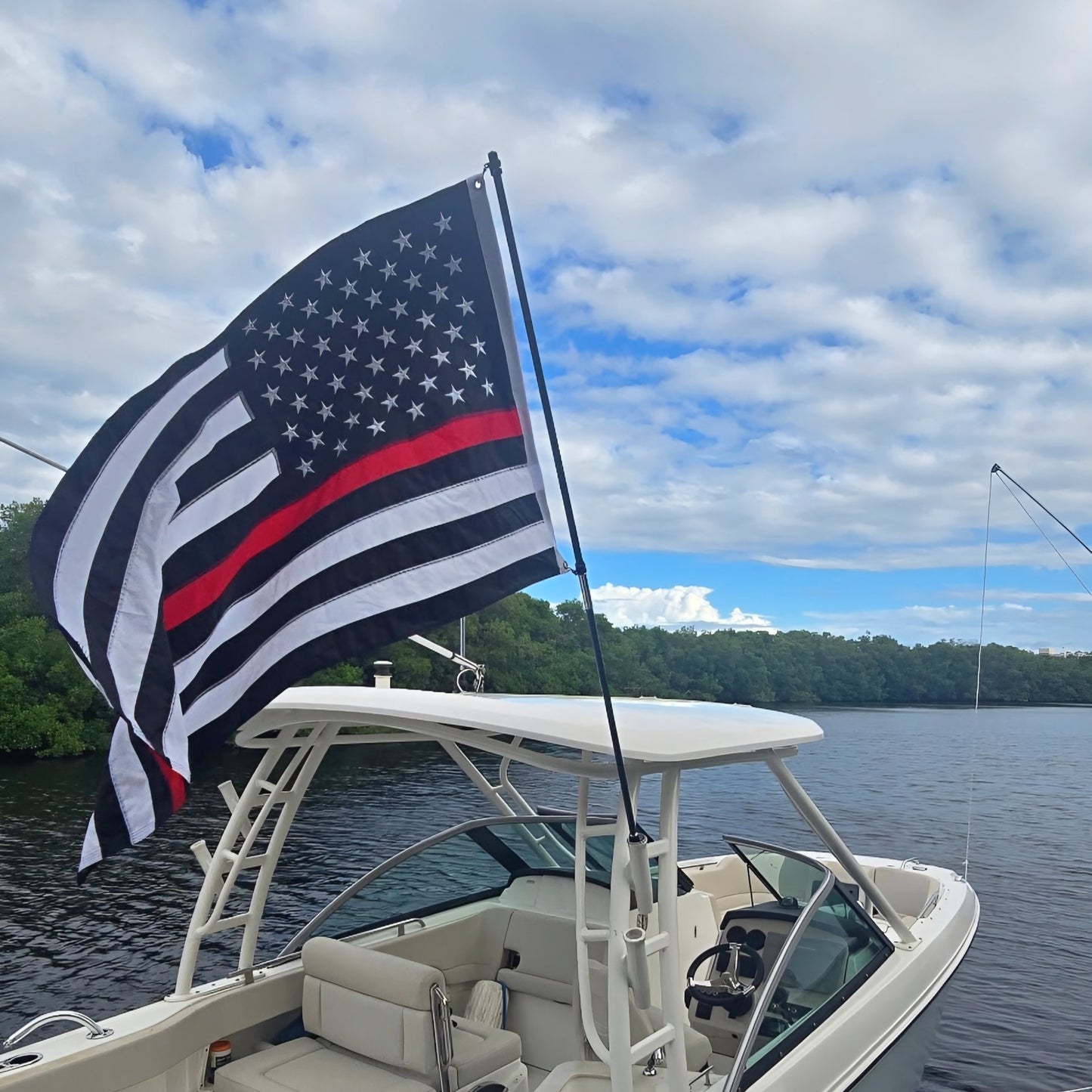 Boat on water with an American flag featuring a red stripe, likely symbolizing firefighters, against a cloudy sky.